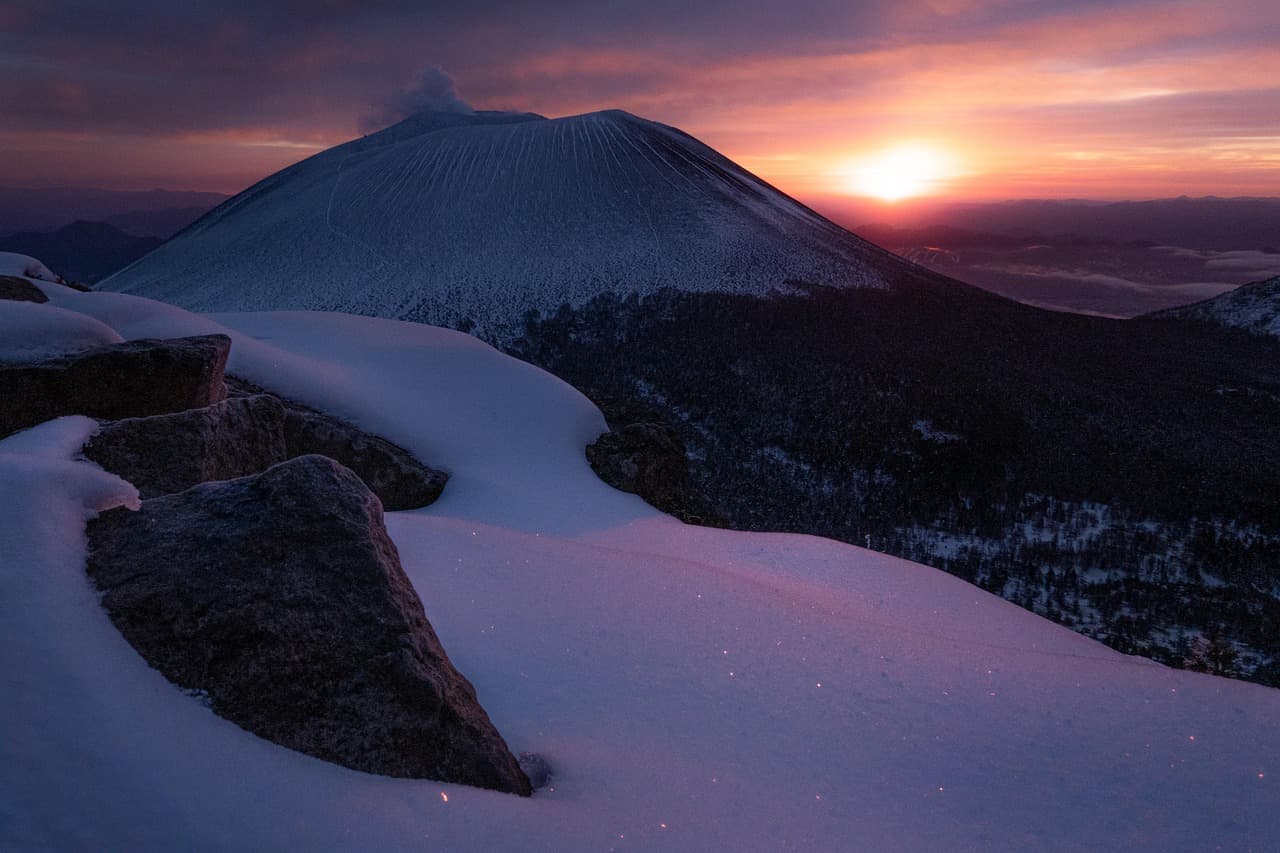 Ośnieżony wulkan dymiący podczas wschodu słońca w zimowych górach.