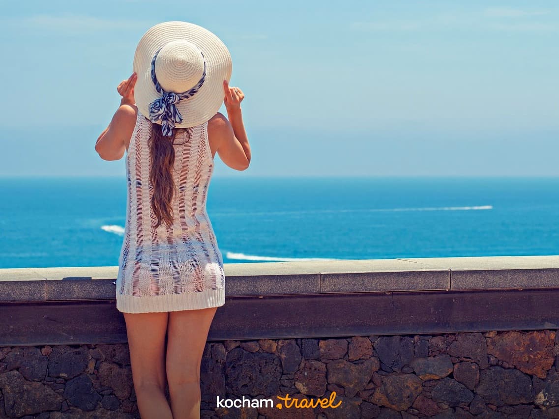 Kobieta w białym kapeluszu podziwiająca lazurowe morze.