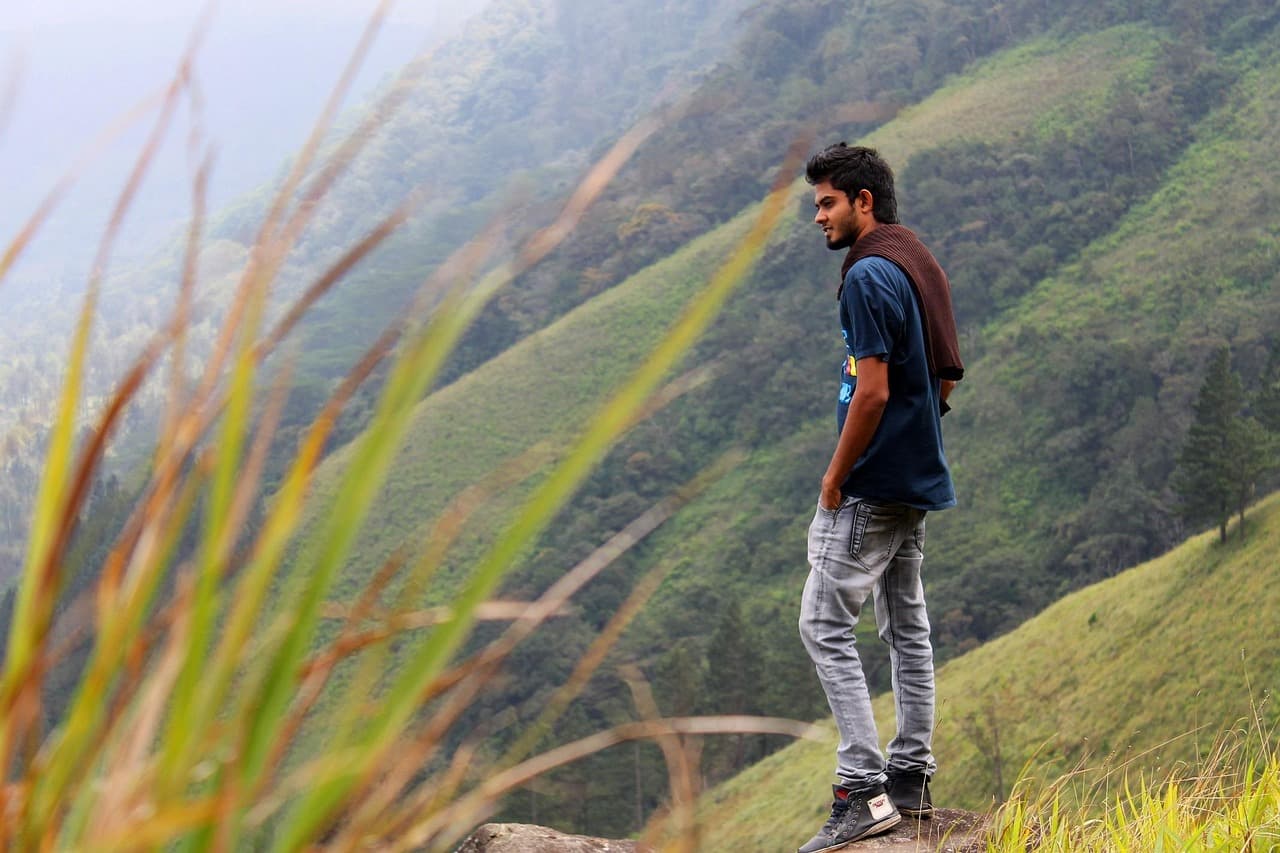 Młody mężczyzna patrzy na mgliste, zielone wzgórza z krawędzi.