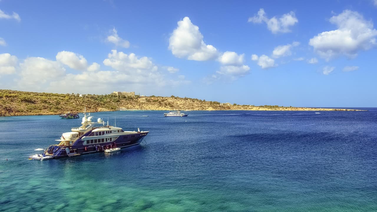 Luksusowy jacht na turkusowych wodach, skaliste wybrzeże, błękitne niebo.