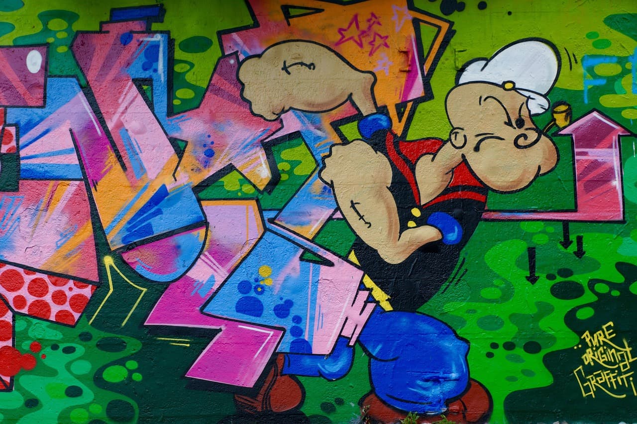 Mural Popeye'a marynarza z muskularnymi ramionami na zielonej ścianie.