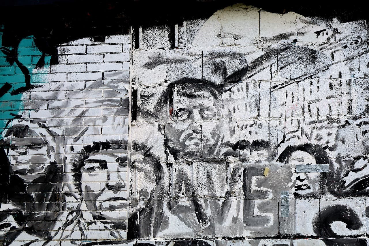 Ekspresyjne graffiti przedstawiające twarze na białej ceglanej ścianie.