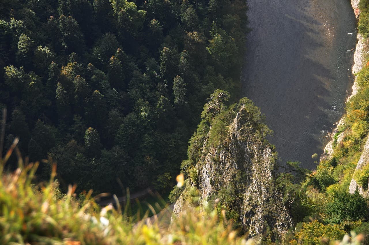 Górski krajobraz z rzeką, zalesionymi zboczami i skalistym klifem.