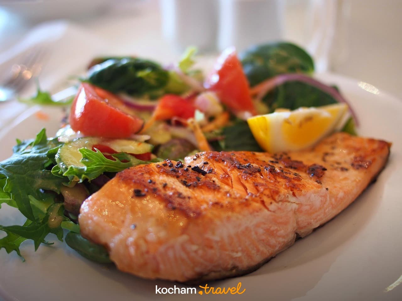 Grillowany łosoś ze świeżą sałatką i cytryną na białym talerzu.