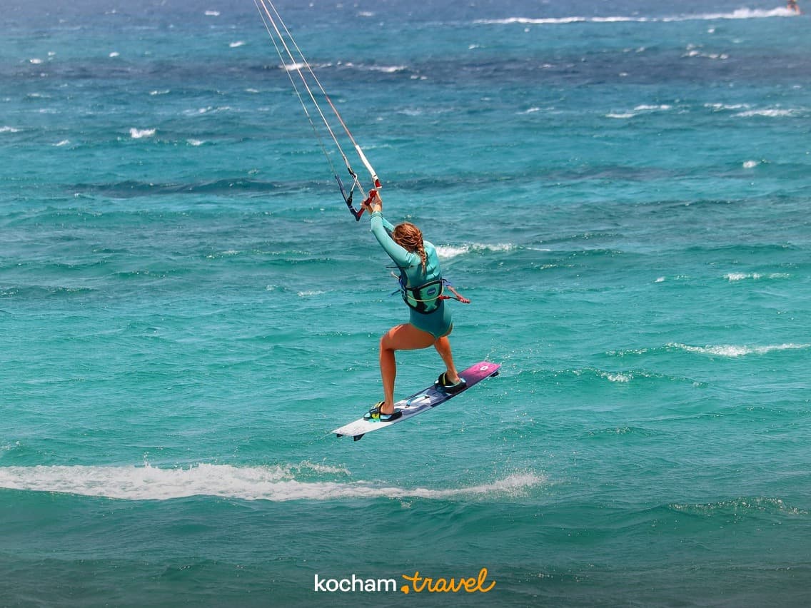 Skacząca kitesurferka na turkusowej wodzie podczas słonecznego dnia.