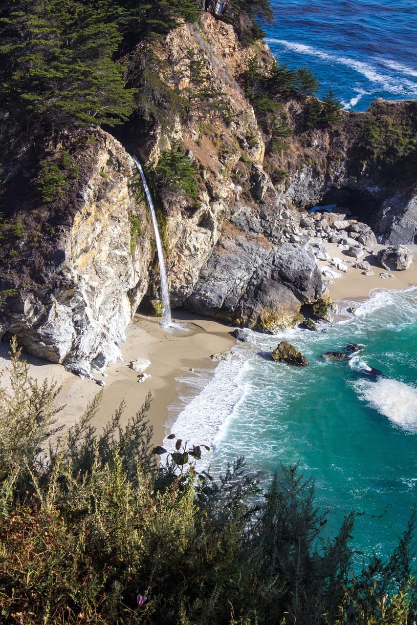 Wodospad McWay Falls spada na piaszczystą plażę i turkusowy ocean.