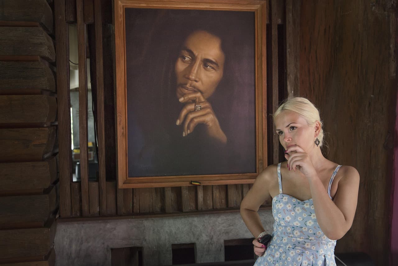 Blondynka w sukience kontempluje obraz Boba Marleya w drewnianym wnętrzu.