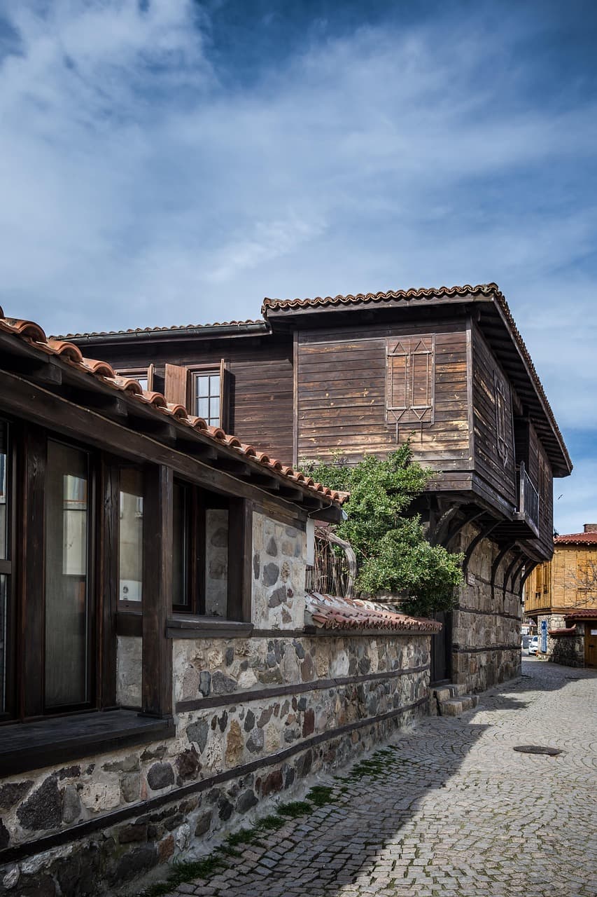 Tradycyjne kamienno-drewniane budynki z czerwonymi dachami przy brukowanej ulicy.