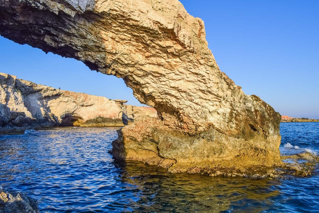 Naturalny most skalny nad błękitnym morzem, skaliste wybrzeże Cypru.