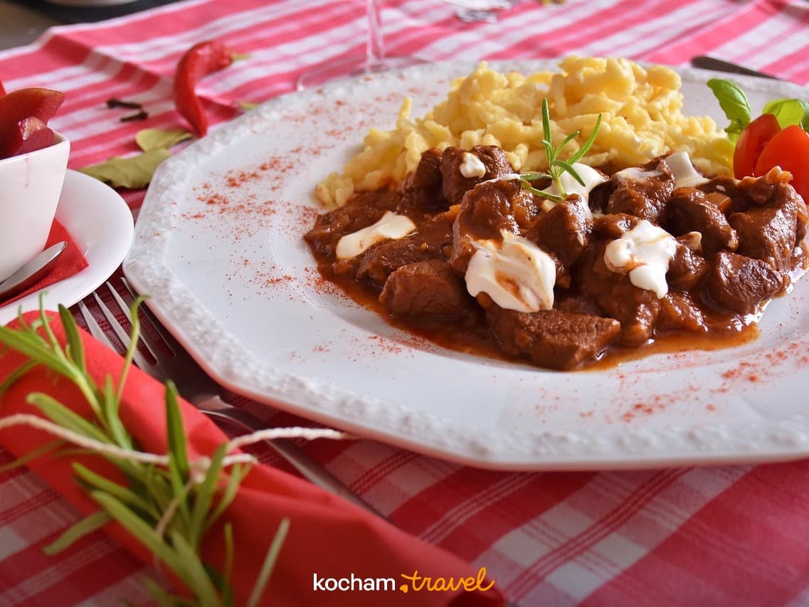 Gulasz z kluskami, kwaśną śmietaną i świeżym rozmarynem na stole.