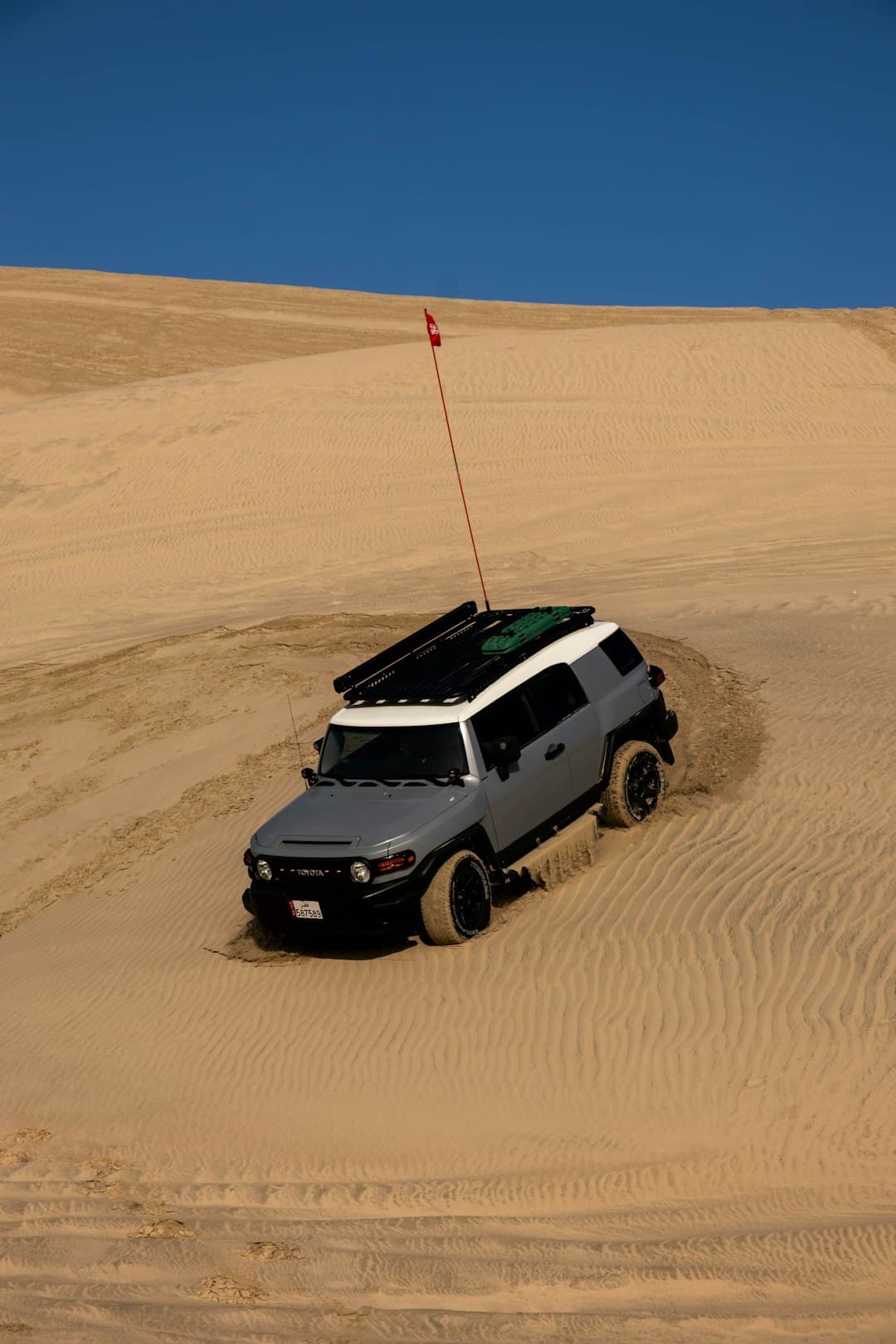 SUV na wydmie piaskowej, pustynny krajobraz, błękitne niebo.