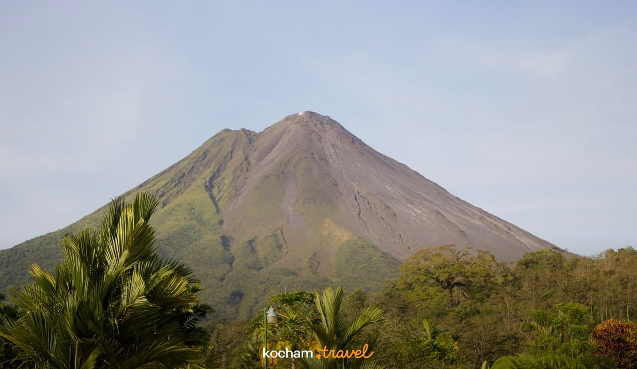 Stożkowy wulkan z zielonymi zboczami i tropikalną roślinnością.