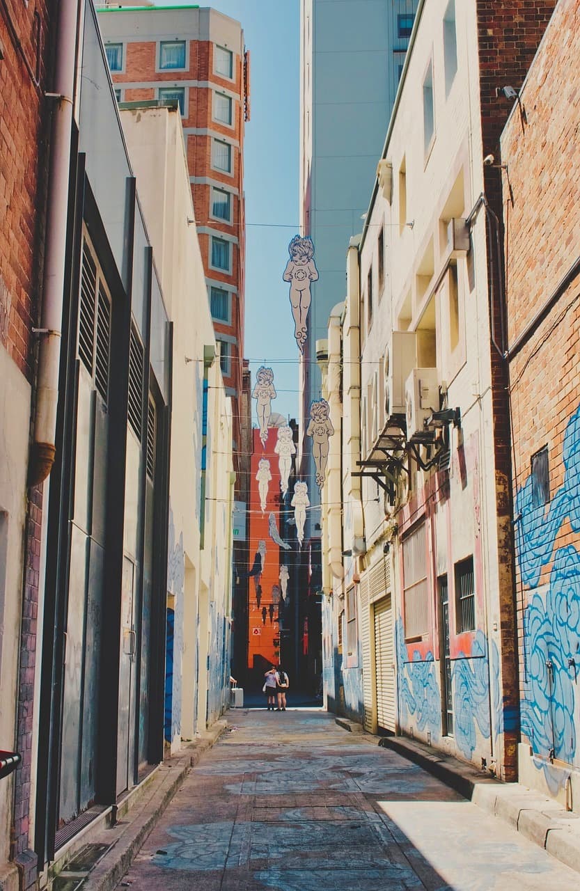 Wąska miejska uliczka z graffiti i wiszącymi figurami aniołków w świetle dziennym.