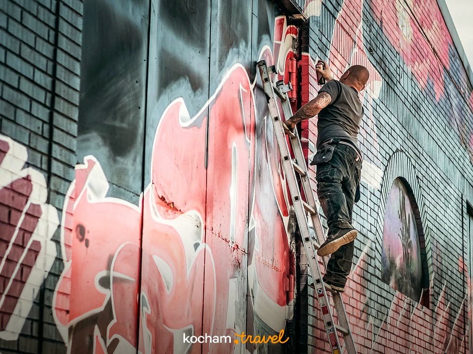 Artysta graffiti malujący czerwoną kompozycję na ceglanej ścianie budynku.