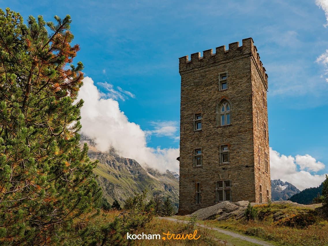 Stara kamienna wieża pośród gór, błękitne niebo, zielone sosny.