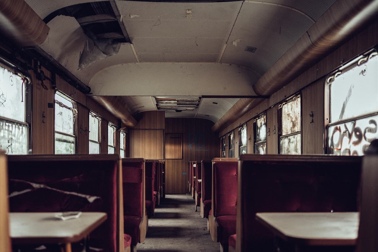 Opuszczony wagon pociągu z czerwonymi siedzeniami i zniszczonymi oknami.