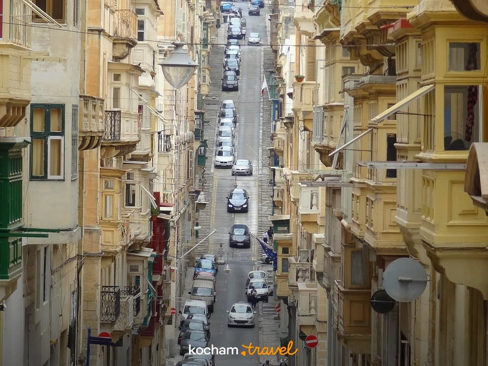 Stroma ulica Valletty z tradycyjnymi, zabudowanymi balkonami i samochodami.