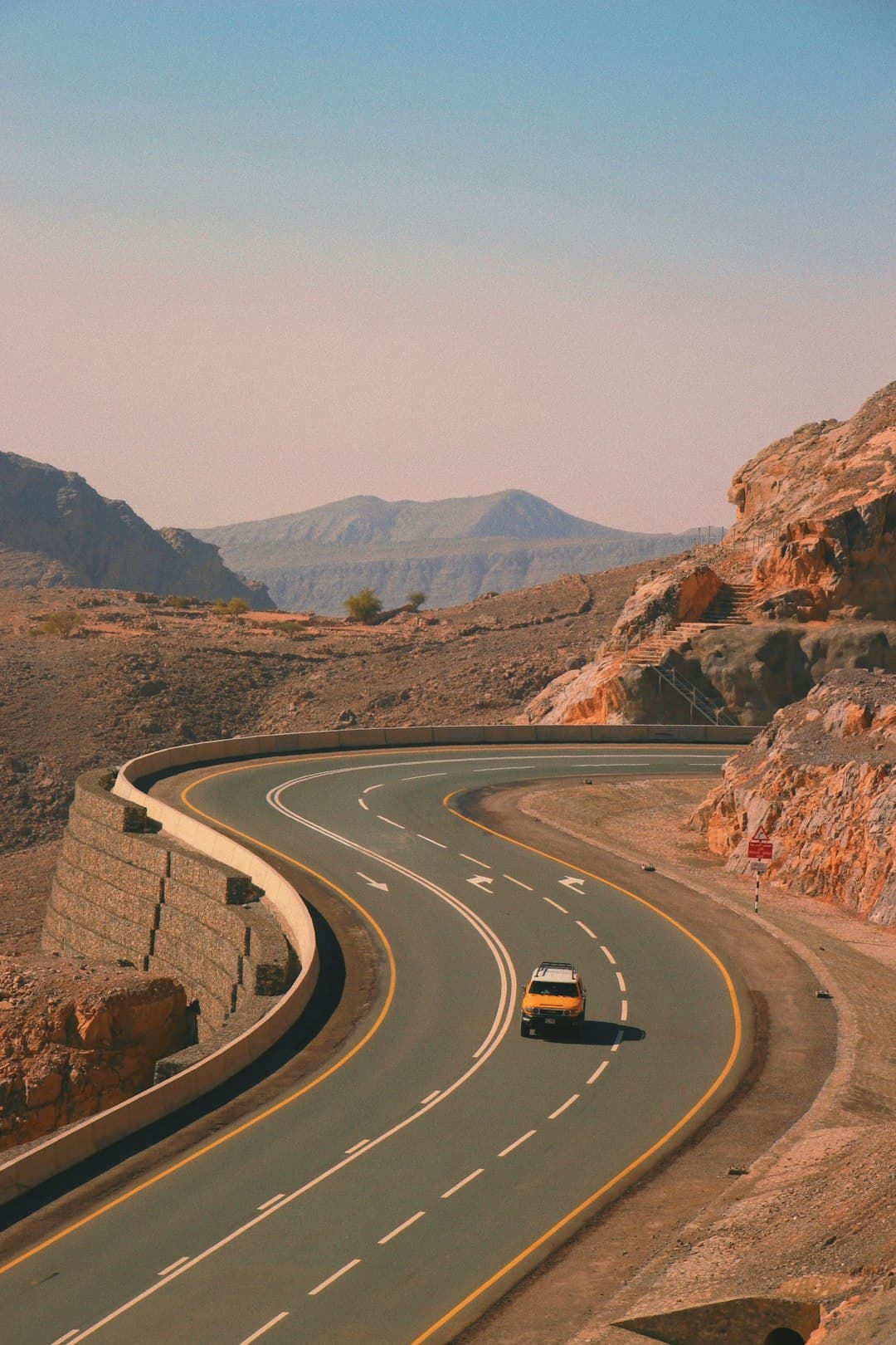 Żółty samochód na górskiej, krętej drodze asfaltowej.