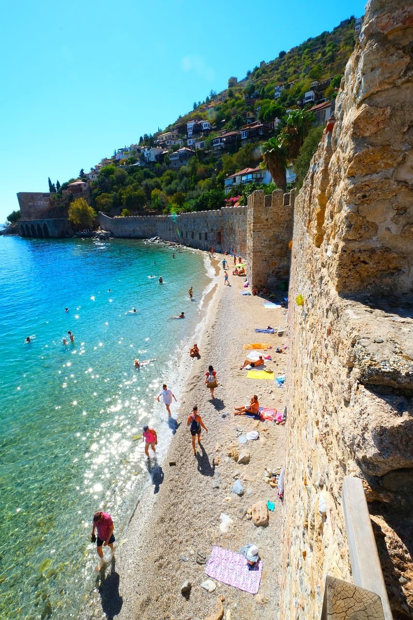 Słoneczna plaża, turkusowe morze, historyczny mur, ludzie