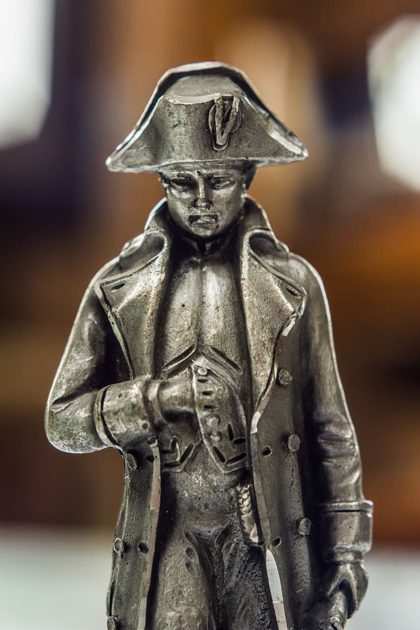 Metalowa figurka Napoleona w kapeluszu i długim płaszczu.